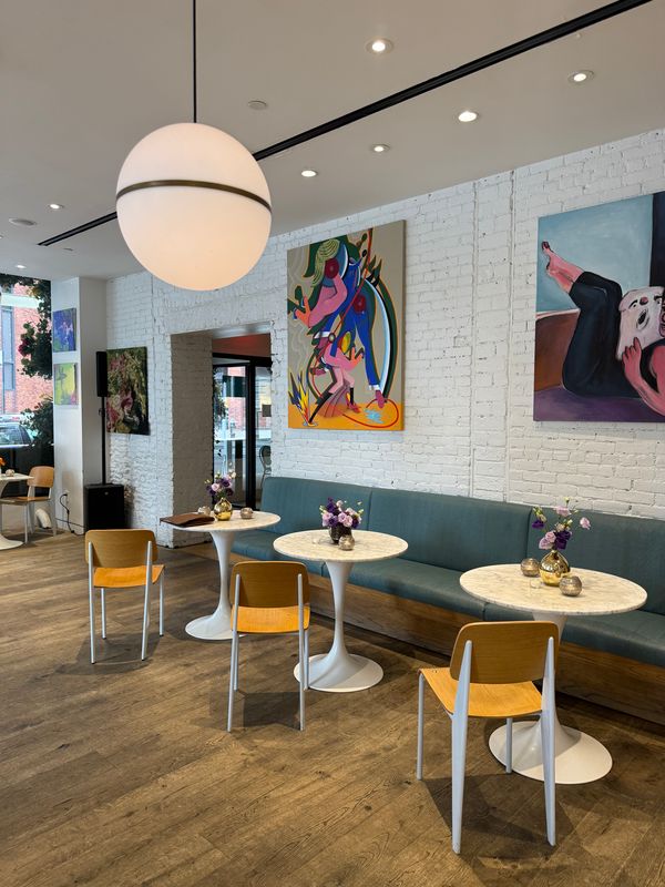 Interior of Spring Cafe Aspen in Greenwich Village with café tables, floral arrangements, colorful artwork, and white brick walls.